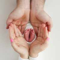 Photo showing a baby's feet in the hands of the mother and father